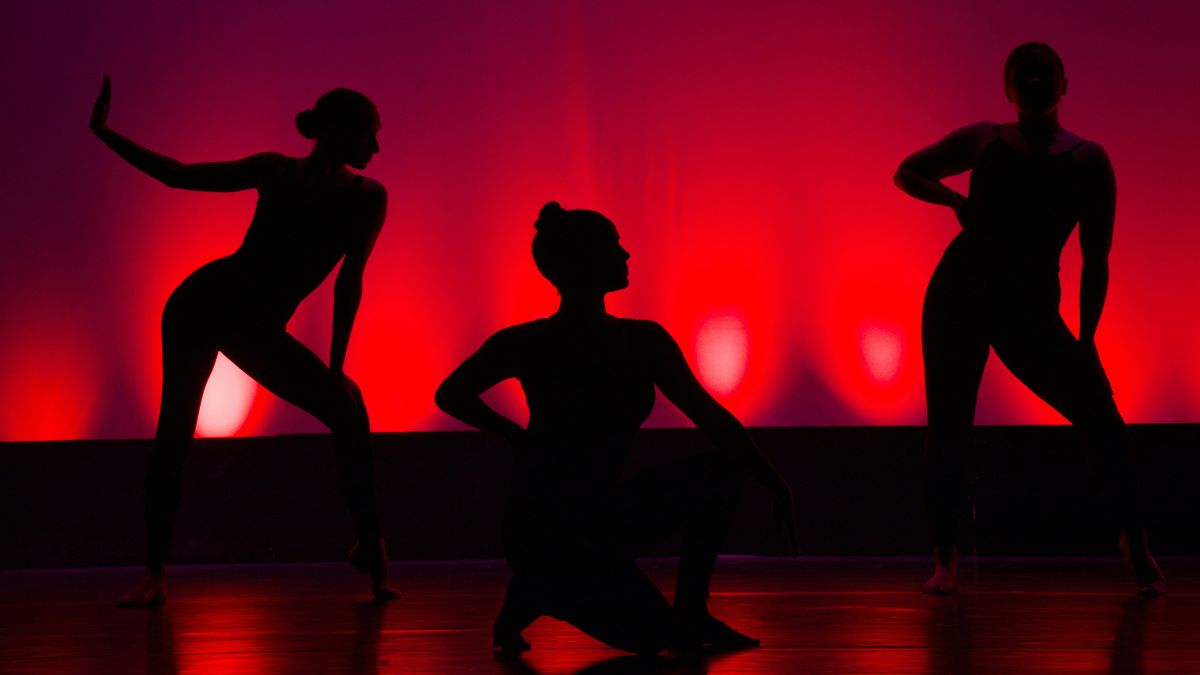 Three dancers on stage with a red background
